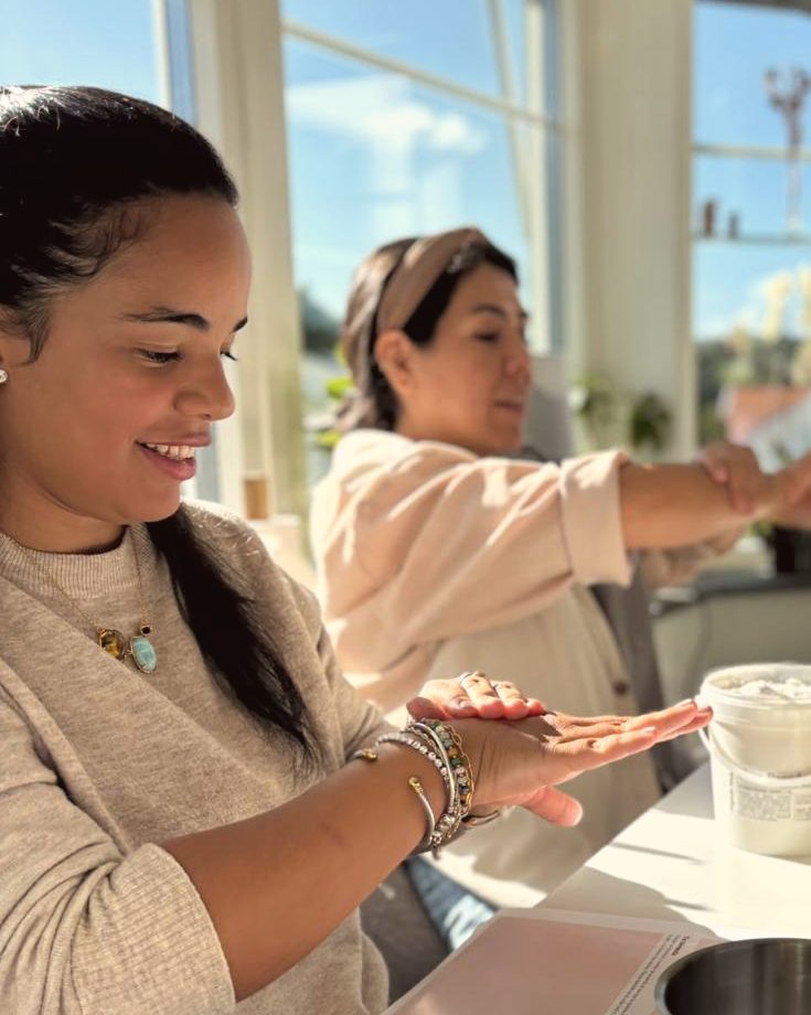Two women applying homemade cream to their hands at a sunny table