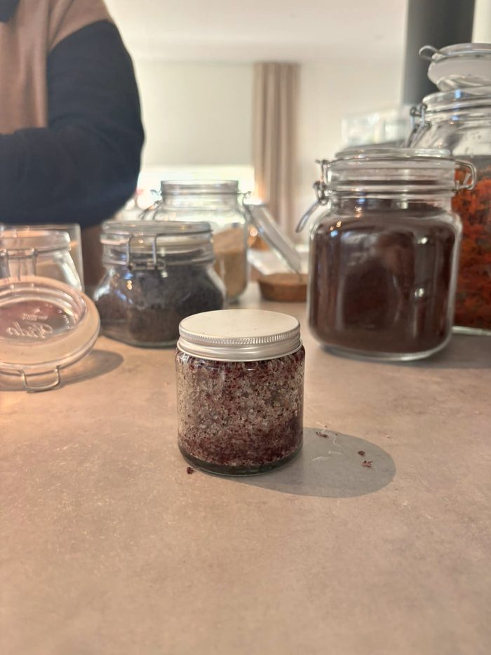 A glass jar of rose-petal body scrub on a kitchen counter