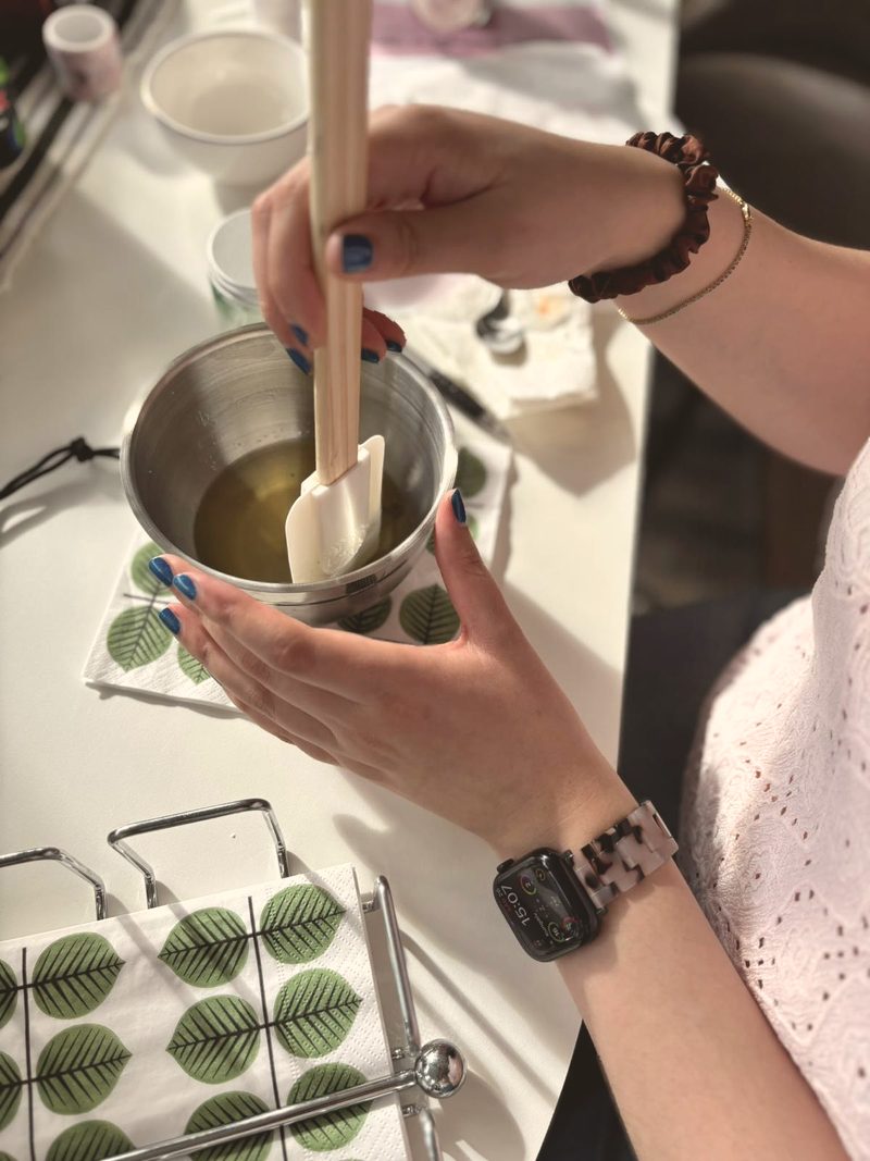 Hands stirring golden oil in a steel bowl on a table with leaf-print napkins