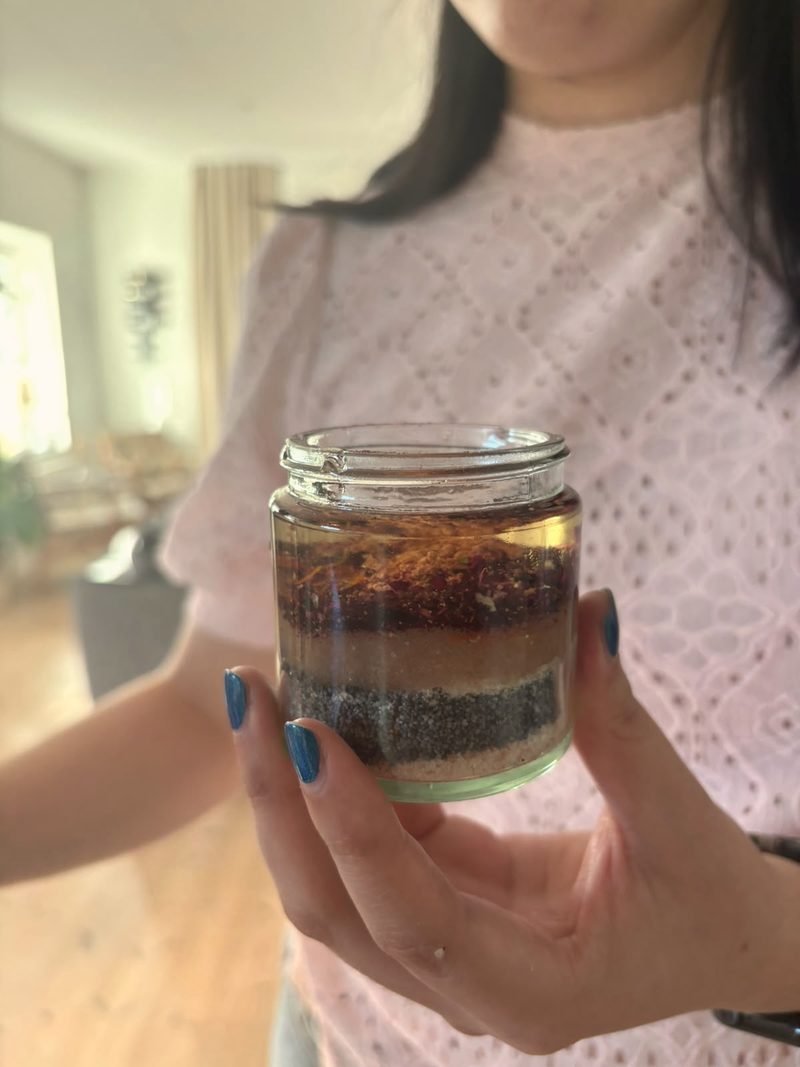 A hand holding a layered jar of homemade scrub